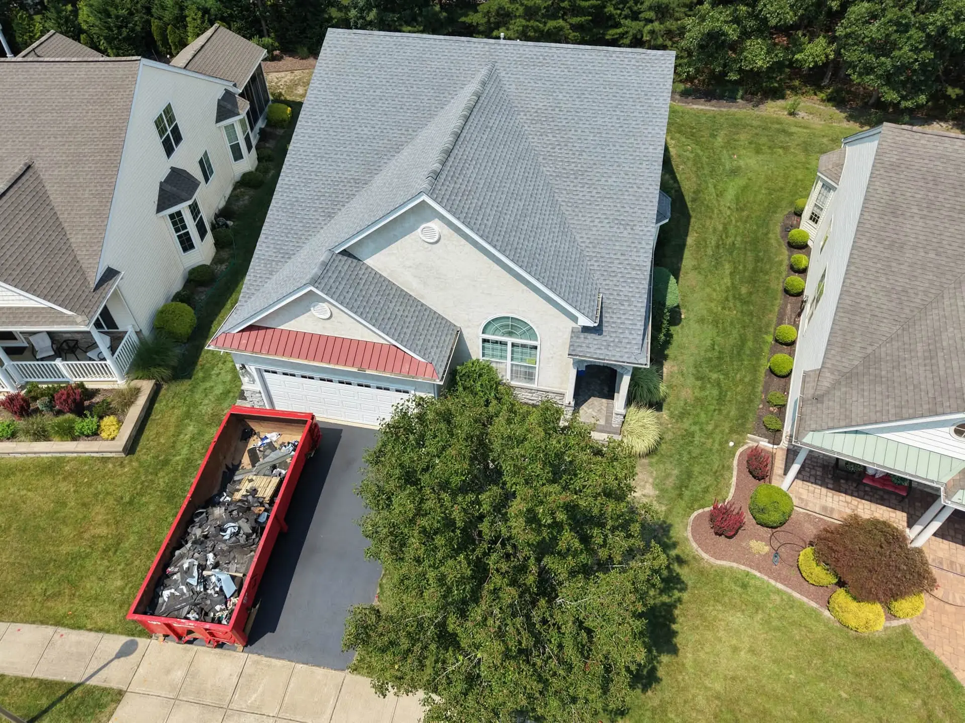 Aerial view of a Forked River, NJ roof replacement in progress with a debris container in the driveway